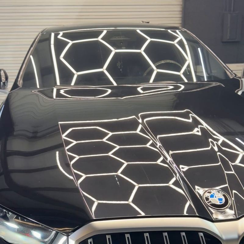 Black BMW hood with a mirror-like gloss reflecting hex lights